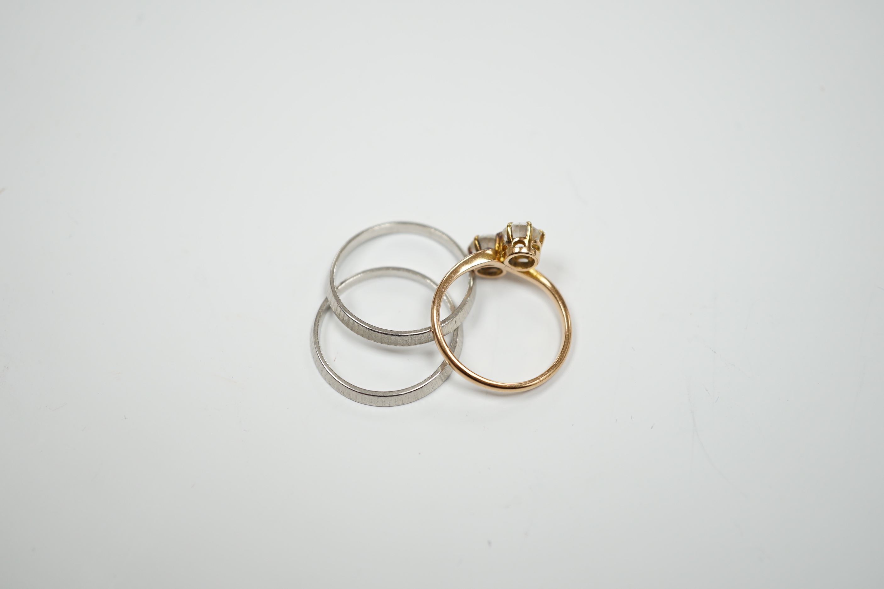 Two white metal bands (stamped platinum) with milled finish, 5.4 grams, together with a 14k and two stone white zircon set crossover ring, gross weight 2.3 grams.